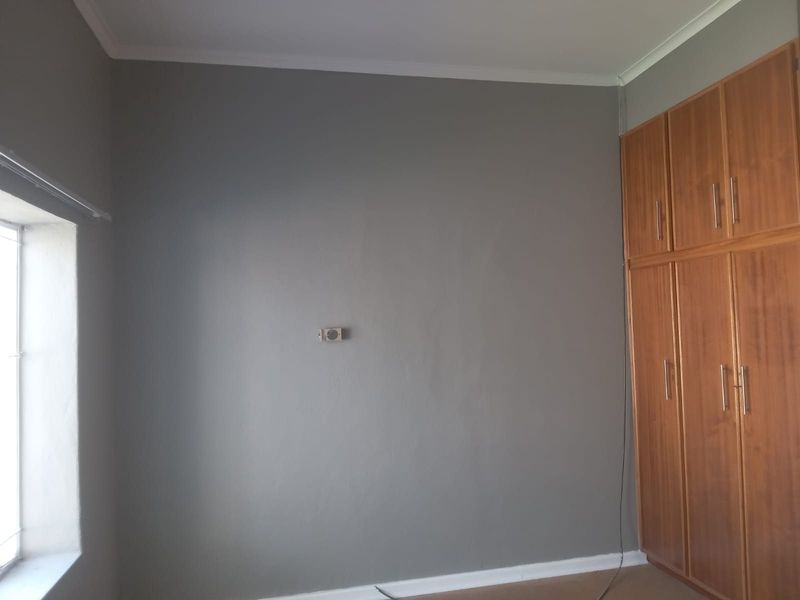 A clean, empty bedroom featuring neutral grey walls, white coving, and integrated wooden built-in cupboards.