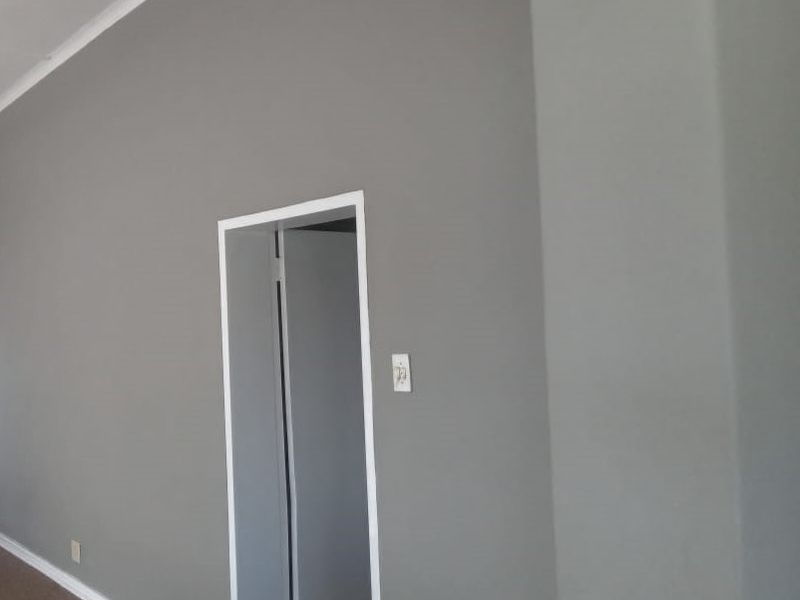 A neutral grey painted hallway featuring white coving and skirting boards with a doorway leading to an adjacent room.