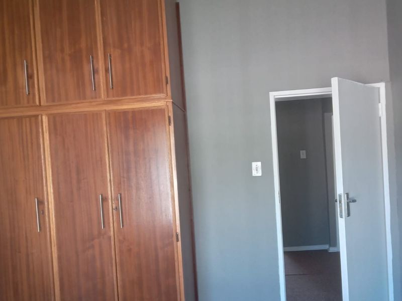 A bedroom featuring built-in wooden cupboards, grey walls, and carpeted flooring, with a doorway leading to an adjacent room.
