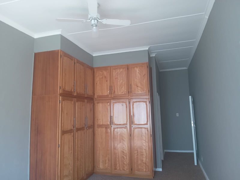 A spacious bedroom featuring extensive built-in wooden cupboards, a ceiling fan, and neutral grey wall finishes.