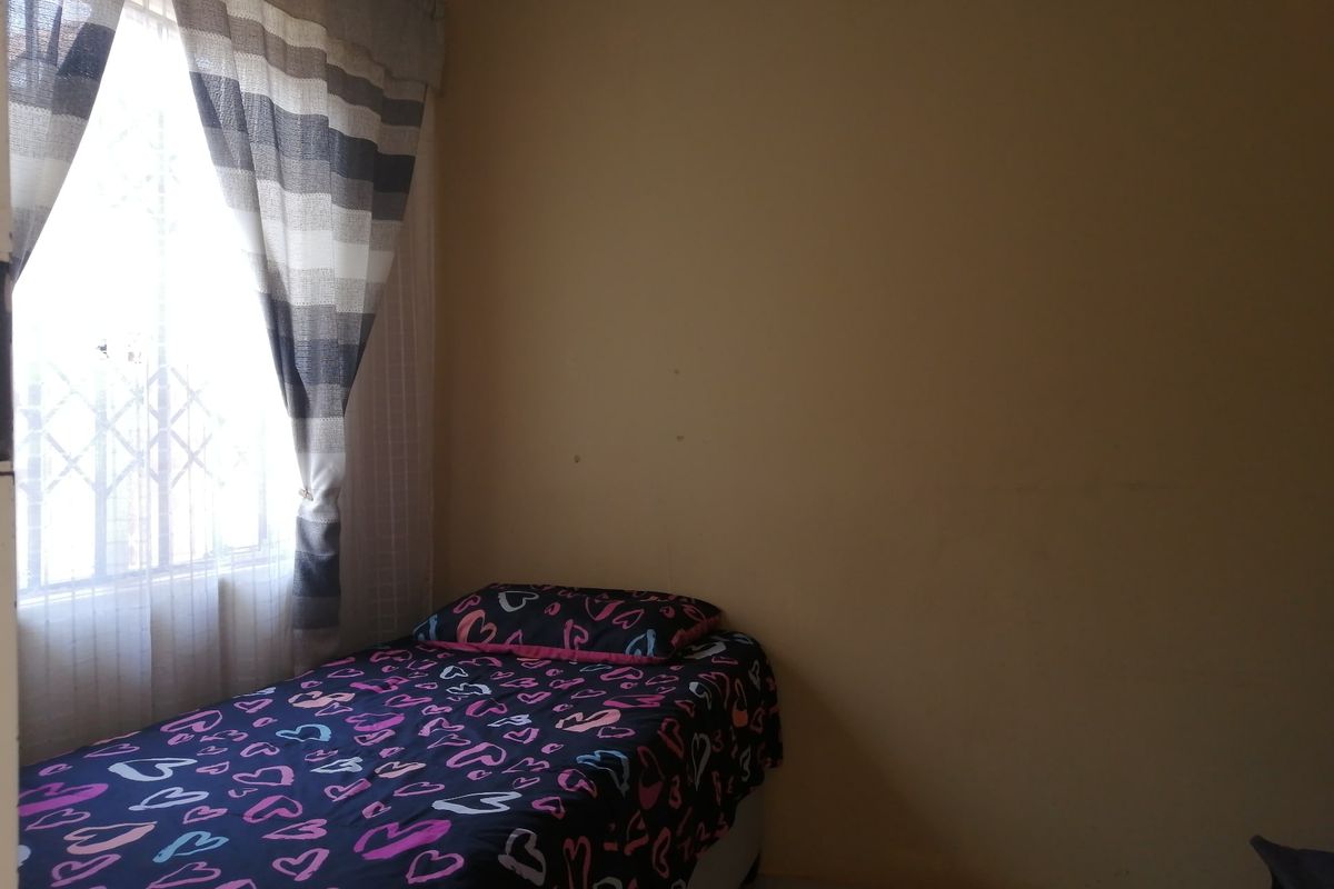 A simple bedroom featuring tiled flooring and a window fitted with a security gate, providing natural light.