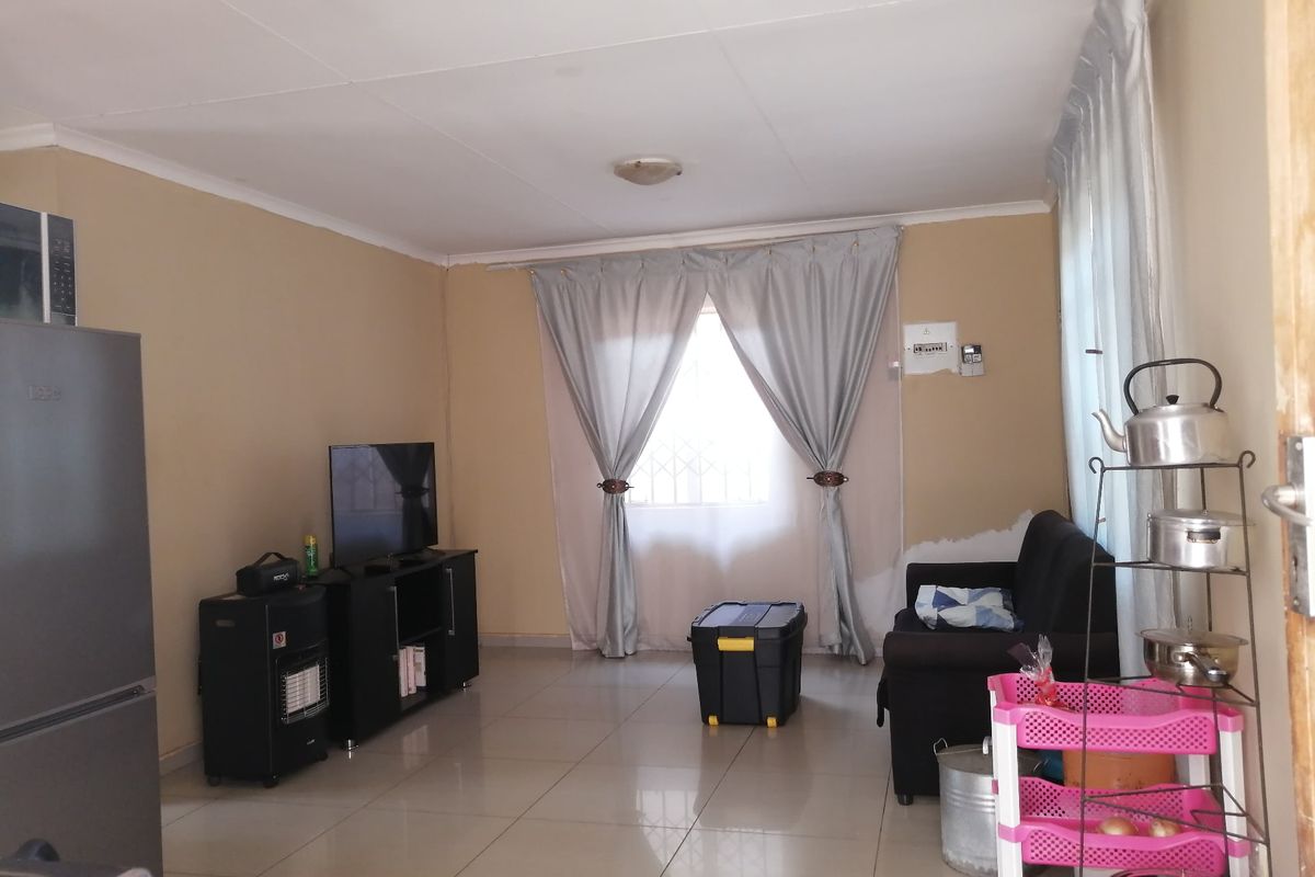 A living room featuring tiled flooring and neutral wall tones, requiring minor cosmetic repairs to the wall finishes near the window area.