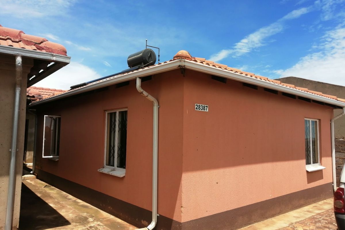 Rear exterior view of the house featuring a solar water heating system, tiled roof, and paved side walkway.