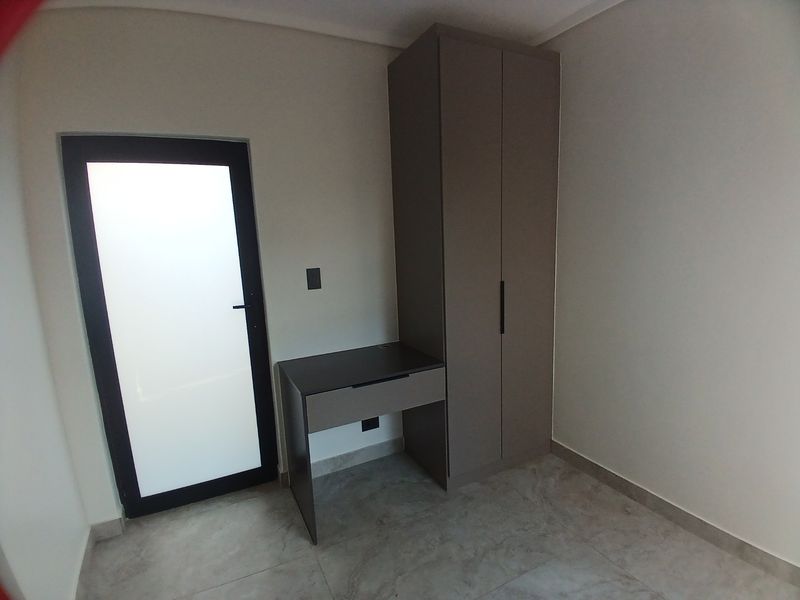 A modern bedroom featuring a built-in wardrobe, integrated desk, tiled flooring, and a frosted glass door providing natural light.