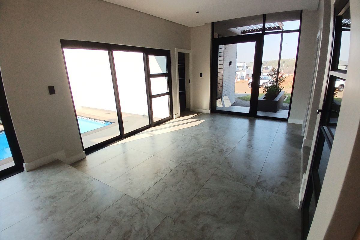 A bright, modern, and empty living area featuring large format floor tiles, recessed lighting, and expansive aluminium sliding doors opening to the pool area.