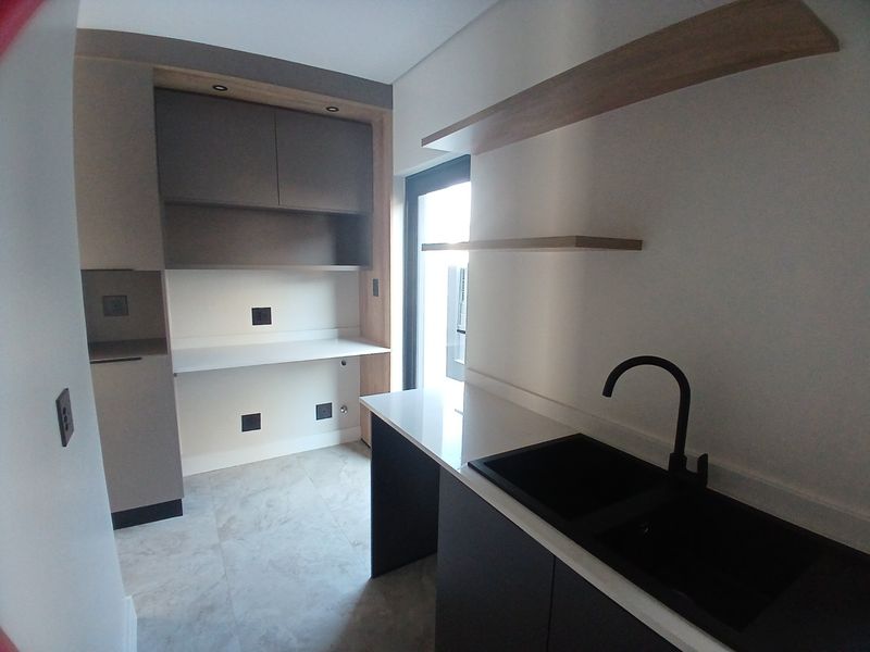 A modern, clean scullery featuring sleek built-in cabinetry, stone countertops, a black sink with matching tap, and floating shelves.