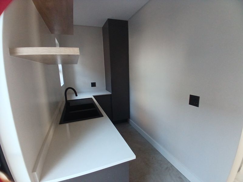 A modern, minimalist scullery featuring dark cabinetry, white stone countertops, a black sink with matching tap, and floating timber shelves.