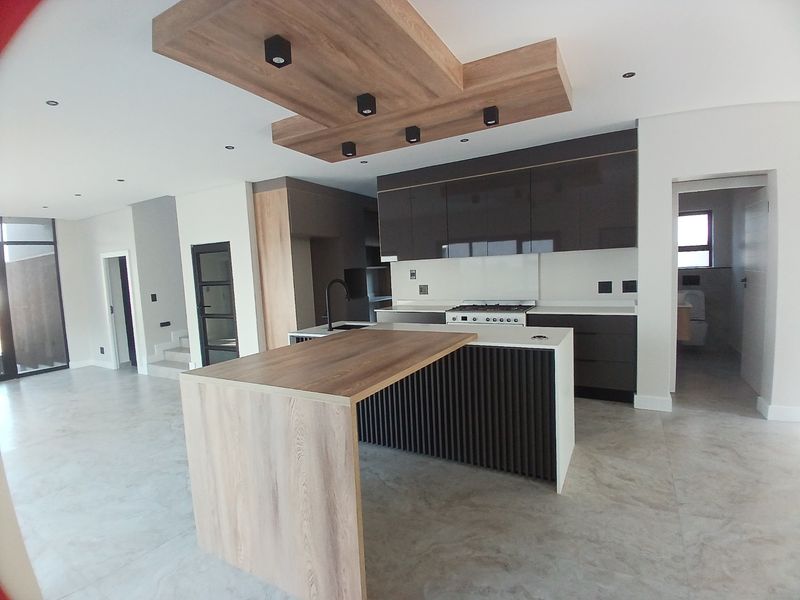 Modern open-plan kitchen featuring a large island, sleek dark cabinetry, stone countertops, gas stove, and a stylish wood-accented ceiling bulkhead.