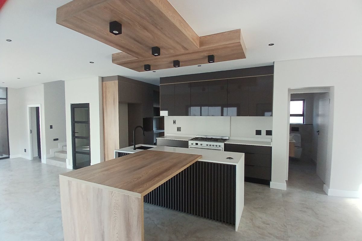 Modern open-plan kitchen featuring high-gloss cabinetry, a central island with a breakfast bar, gas stove, and a stylish wood-accented recessed ceiling feature.