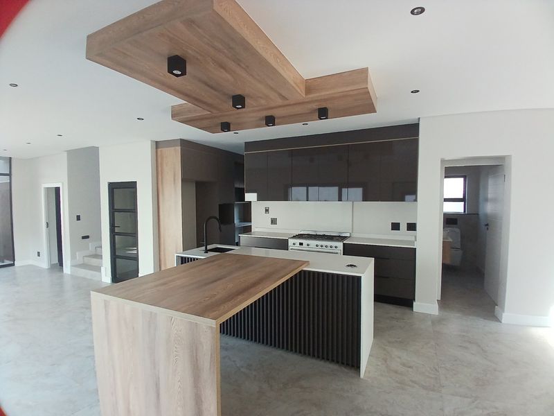 Modern open-plan kitchen featuring high-gloss cabinetry, a central island with a breakfast bar, gas stove, and a stylish wood-accented recessed ceiling feature.