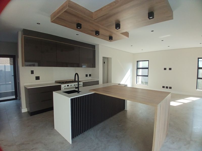 Modern open-plan kitchen featuring a large island with integrated breakfast bar, sleek cabinetry, gas cooktop, and a stylish feature ceiling bulkhead.