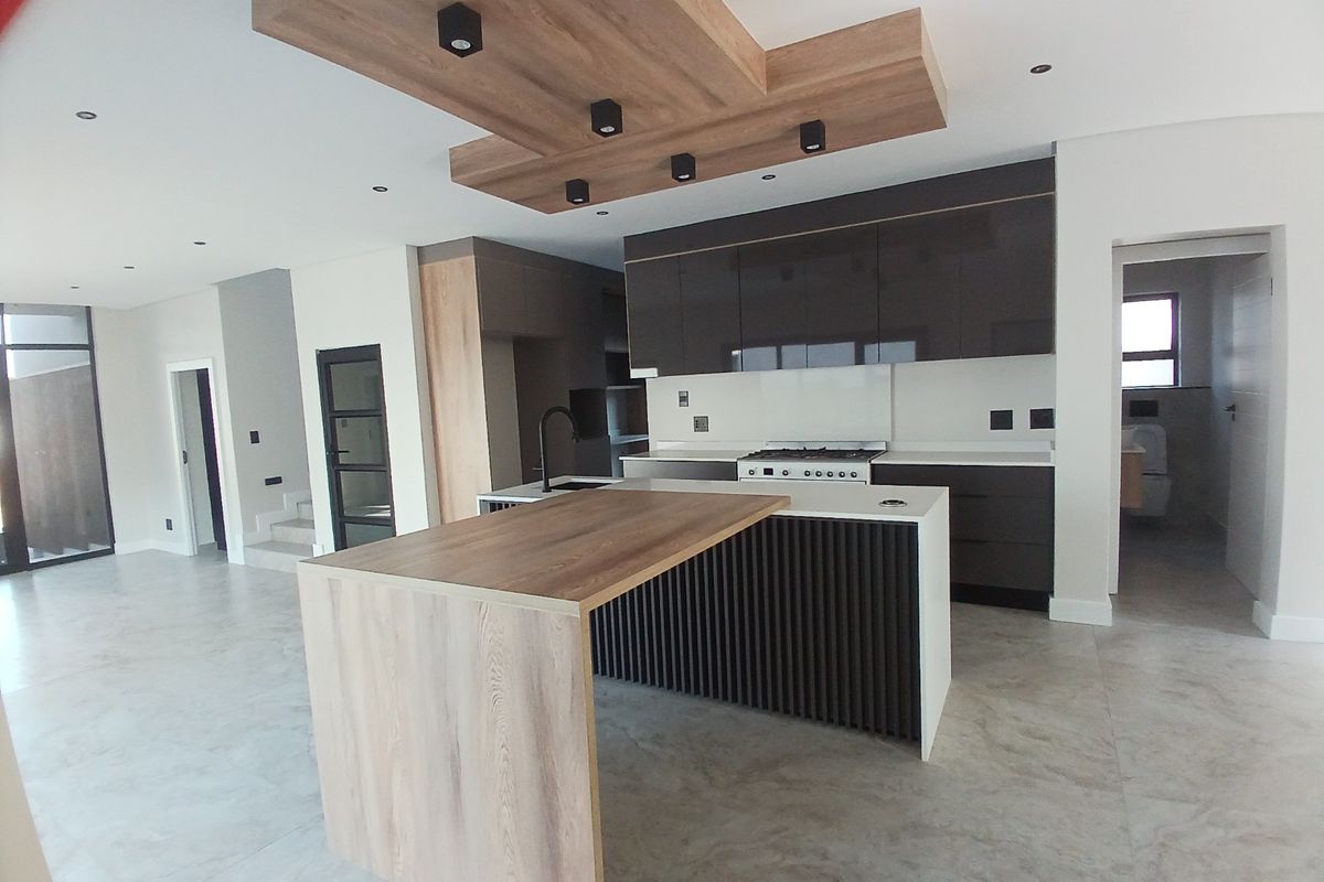 Modern open-plan kitchen featuring a large island, sleek dark cabinetry, stone countertops, gas stove, and a stylish wood-accented ceiling bulkhead.