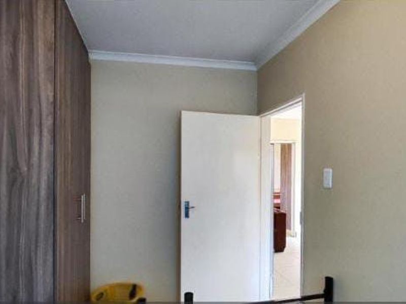 A simple bedroom interior featuring a built-in wooden wardrobe and neutral wall finishes, providing a clean and functional space.