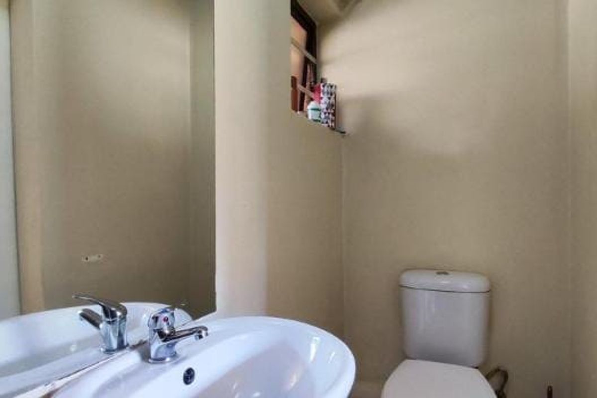 A functional guest bathroom featuring a pedestal basin, chrome mixer tap, wall-mounted mirror, and a standard toilet.