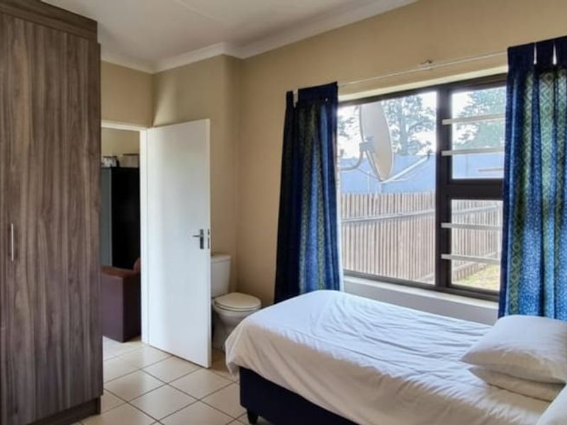 A bedroom featuring built-in cupboards, tiled flooring, and a window with security bars, providing a functional and well-lit living space.