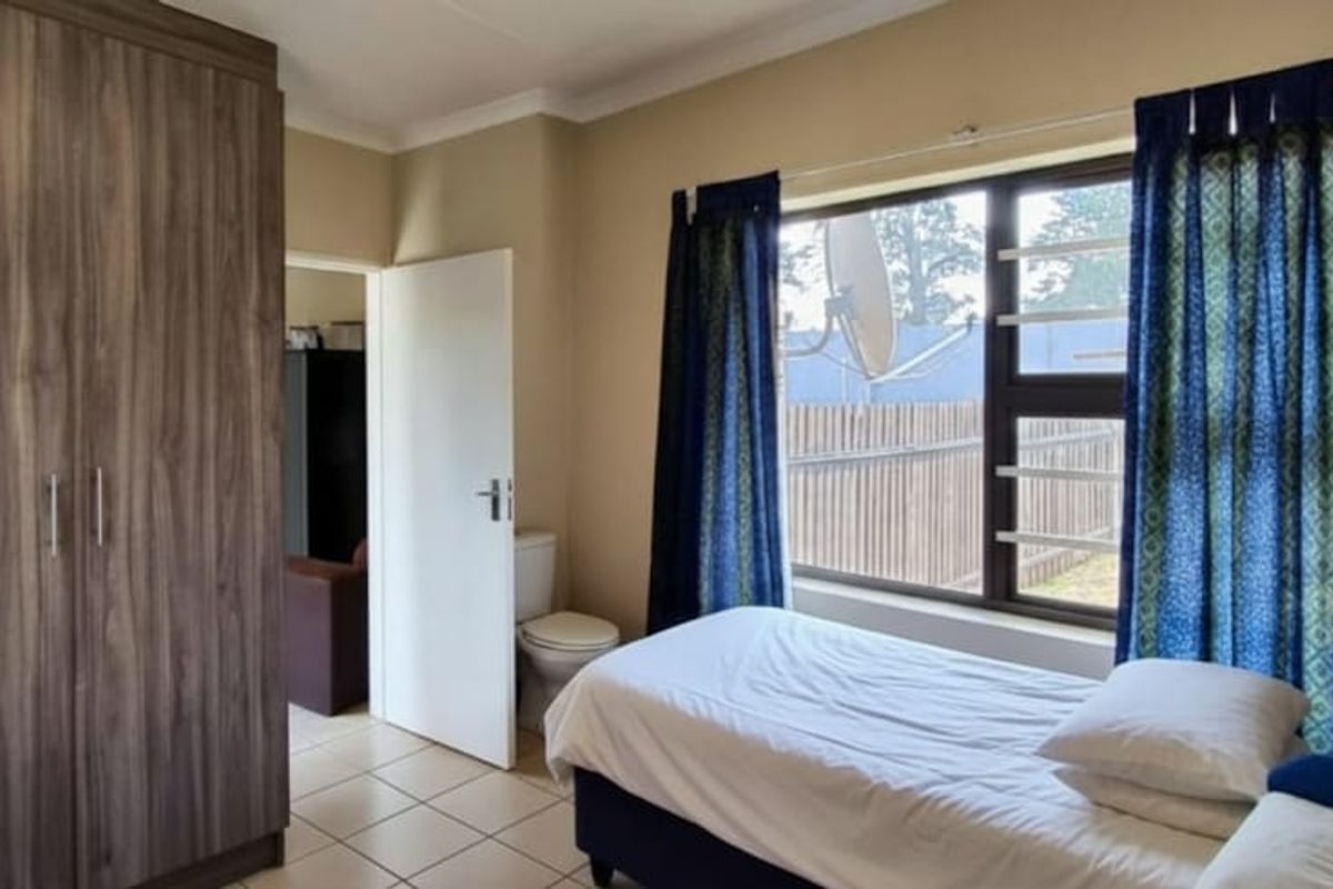 A bedroom featuring built-in cupboards, tiled flooring, and a window with security bars, providing a functional and well-lit living space.