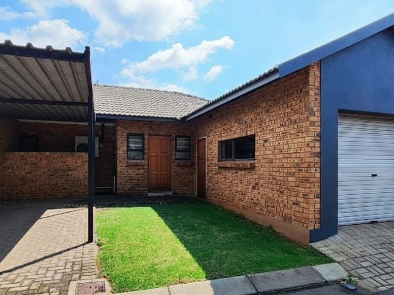 Front exterior view of a face brick townhouse featuring a single garage with a roller door, a covered carport, and a small front lawn.