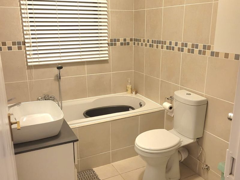 A well-maintained bathroom featuring a built-in bathtub, vessel sink vanity, and neutral floor-to-ceiling tiling with a decorative mosaic border.
