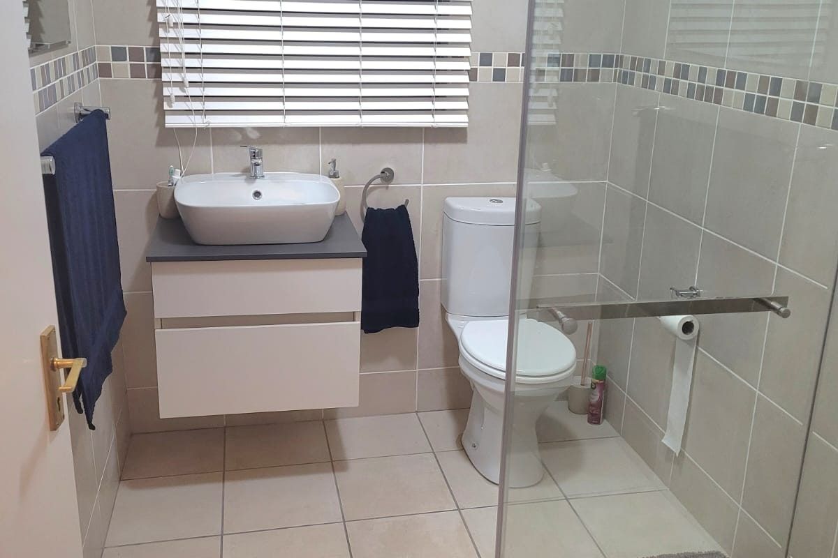 A modern bathroom featuring a wall-mounted vanity with a vessel sink, a glass-enclosed shower, and neutral floor-to-ceiling tiling.