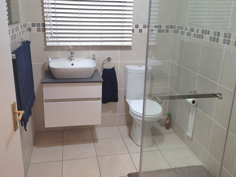 A modern bathroom featuring a wall-mounted vanity with a vessel sink, a glass-enclosed shower, and neutral floor-to-ceiling tiling.