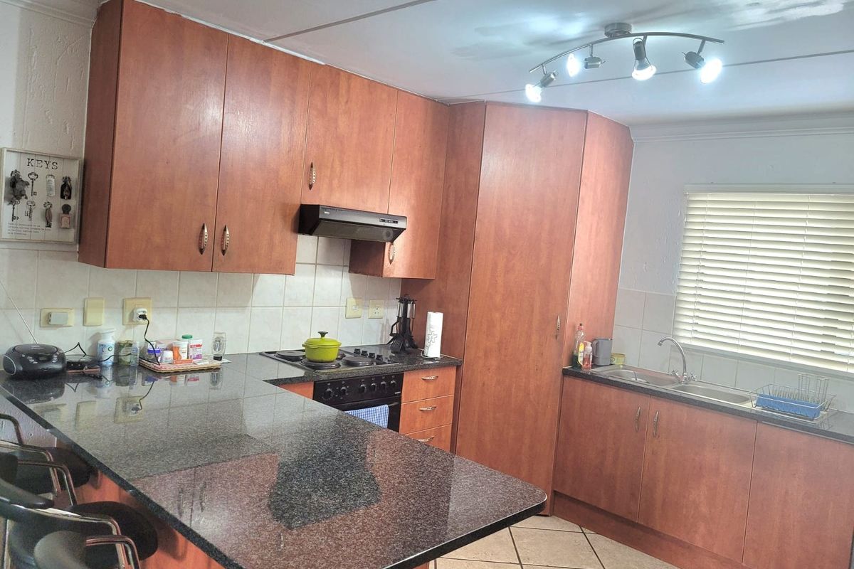 Functional kitchen featuring wood-look laminate cabinetry, granite countertops, built-in oven with extractor fan, and a breakfast bar peninsula.