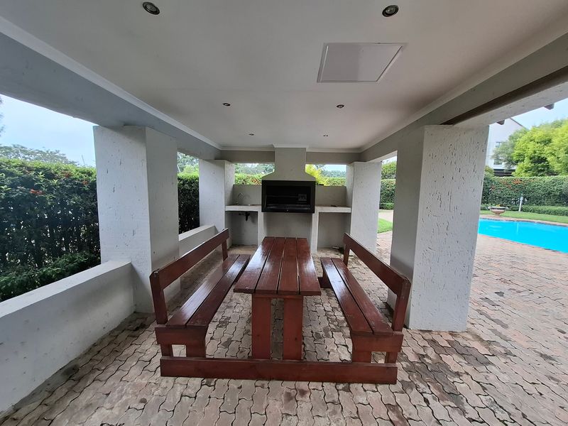 Covered outdoor patio area featuring a built-in braai, sink, and recessed lighting, overlooking the swimming pool and garden.