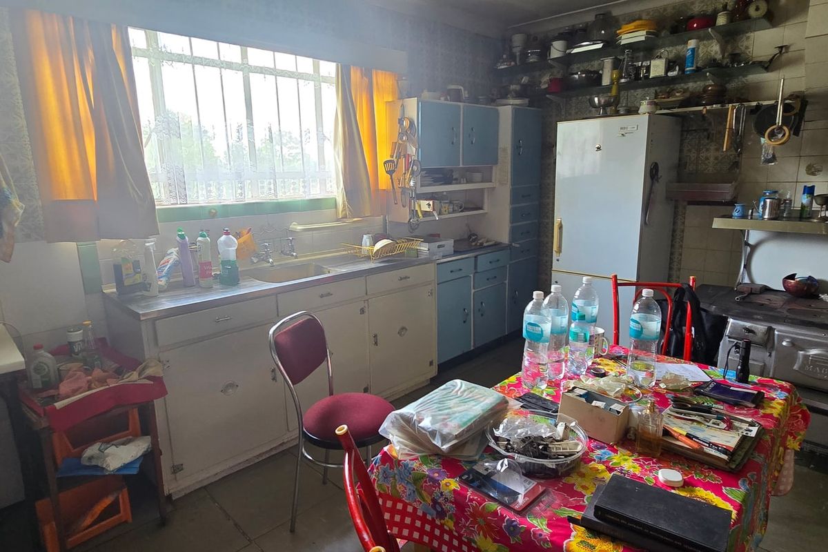 A dated kitchen featuring original cabinetry, a vintage wood-burning stove, and a tiled splashback, offering significant potential for a modern renovation.