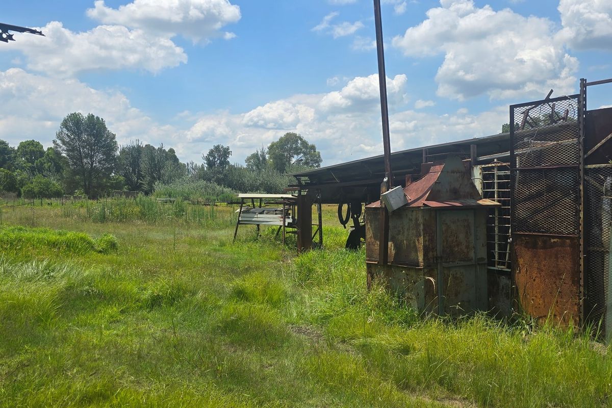 A view of the rear property grounds featuring a dilapidated metal shed structure and overgrown grass area.