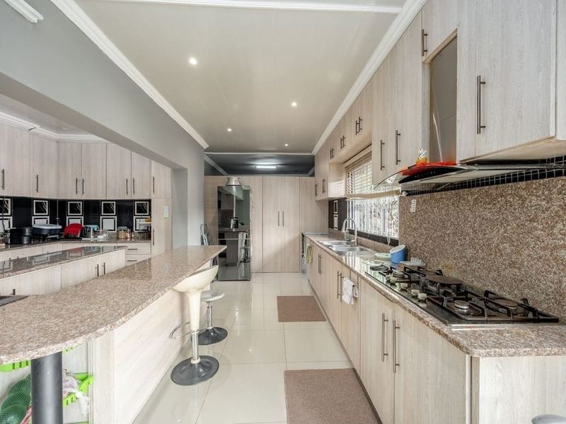 Spacious kitchen featuring light wood cabinetry, granite countertops, a built-in gas hob with extractor, and tiled flooring throughout.