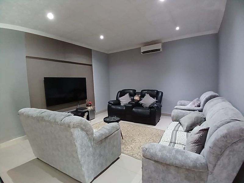 A well-maintained living room featuring tiled flooring, recessed downlighting, and a wall-mounted split-system air conditioning unit.
