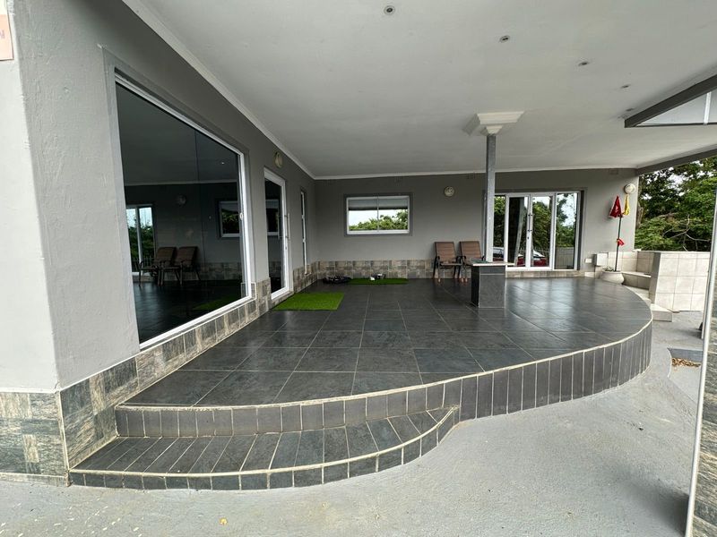 A spacious covered patio featuring dark tiled flooring, recessed lighting, and multiple sliding glass door access points to the interior living areas.