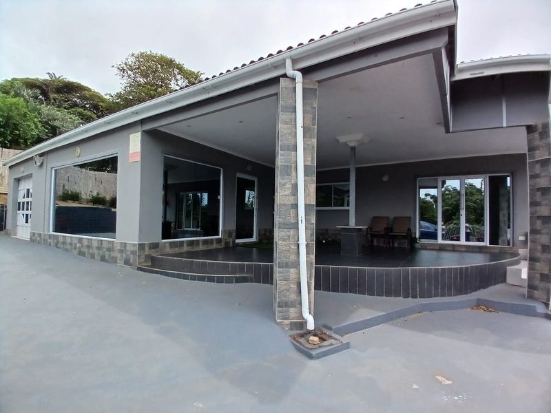 A spacious covered rear patio featuring stone-clad pillars, tiled flooring, and large sliding glass doors providing access to the interior living spaces.