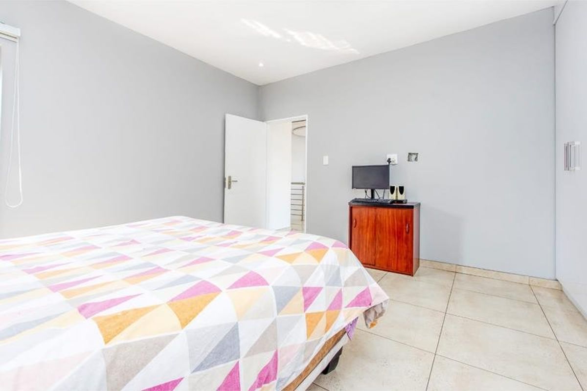 A bright bedroom featuring neutral grey walls, tiled flooring, and built-in storage cupboards.