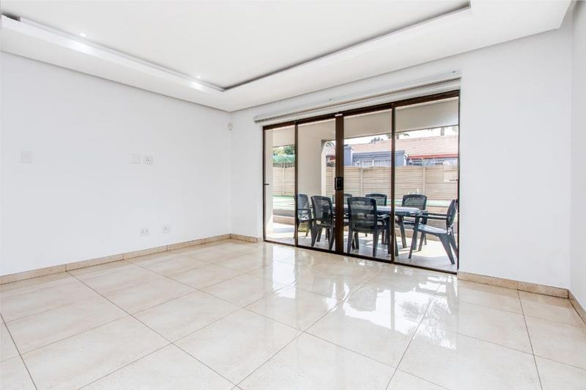A bright, empty living room featuring large sliding glass doors that open onto an outdoor patio area, finished with neutral floor tiles.