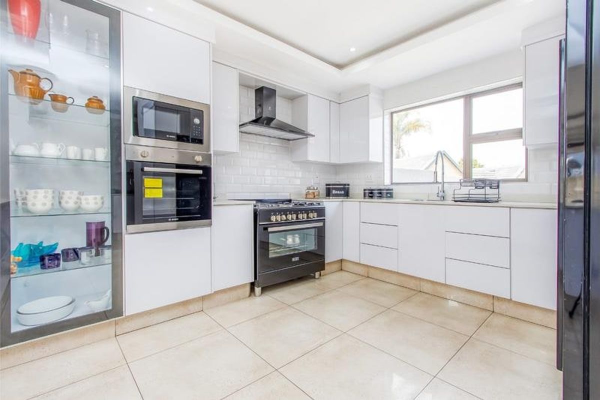 Modern kitchen featuring white cabinetry, subway tile backsplash, high-end built-in appliances, and tiled flooring with a glass display cabinet.