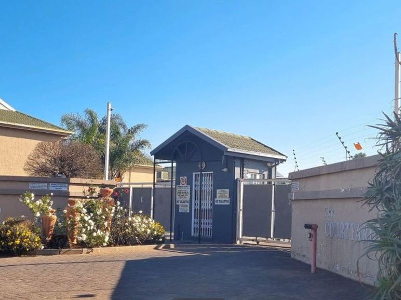 The entrance to The Courtyard apartment complex, featuring a secure gated access point, guard house, and perimeter wall with electric fencing.