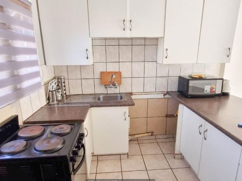 Compact kitchen featuring laminate countertops, tiled backsplash, and white cabinetry. The space requires maintenance to address missing tiles and cabinet doors.