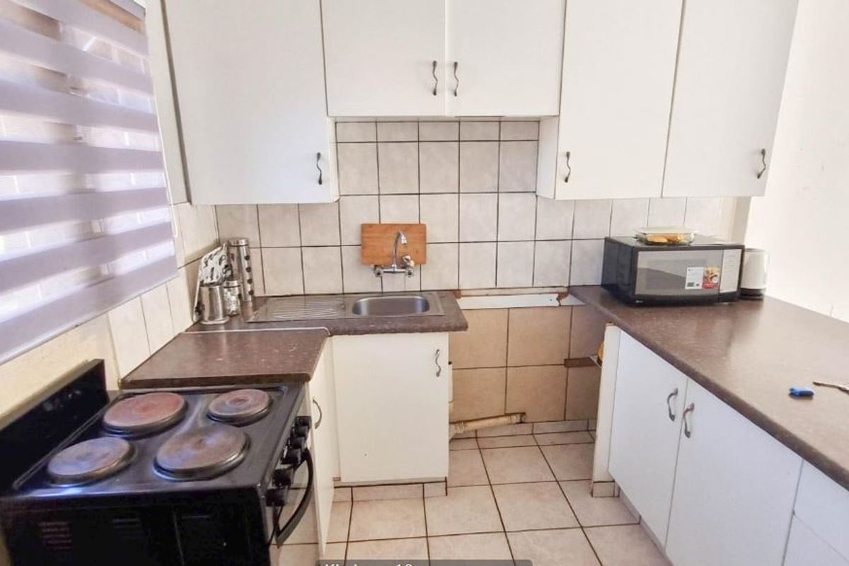 Compact kitchen featuring laminate countertops, tiled backsplash, and white cabinetry. The space requires maintenance to address missing tiles and cabinet doors.
