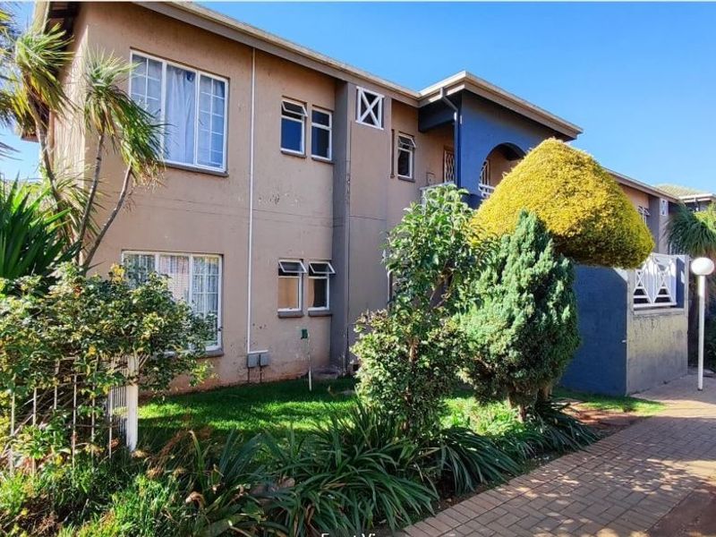 Exterior view of a multi-story apartment building featuring a paved walkway and established garden area.