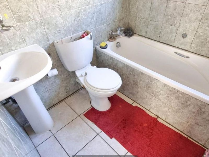 A functional bathroom featuring a pedestal basin, standard toilet, and a built-in bathtub with full-height wall tiling.
