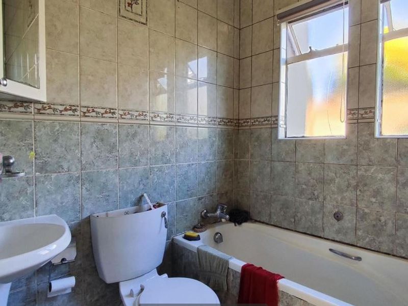 A functional bathroom featuring a pedestal basin, bathtub, and tiled walls. The space is dated and would benefit from modern finishes.