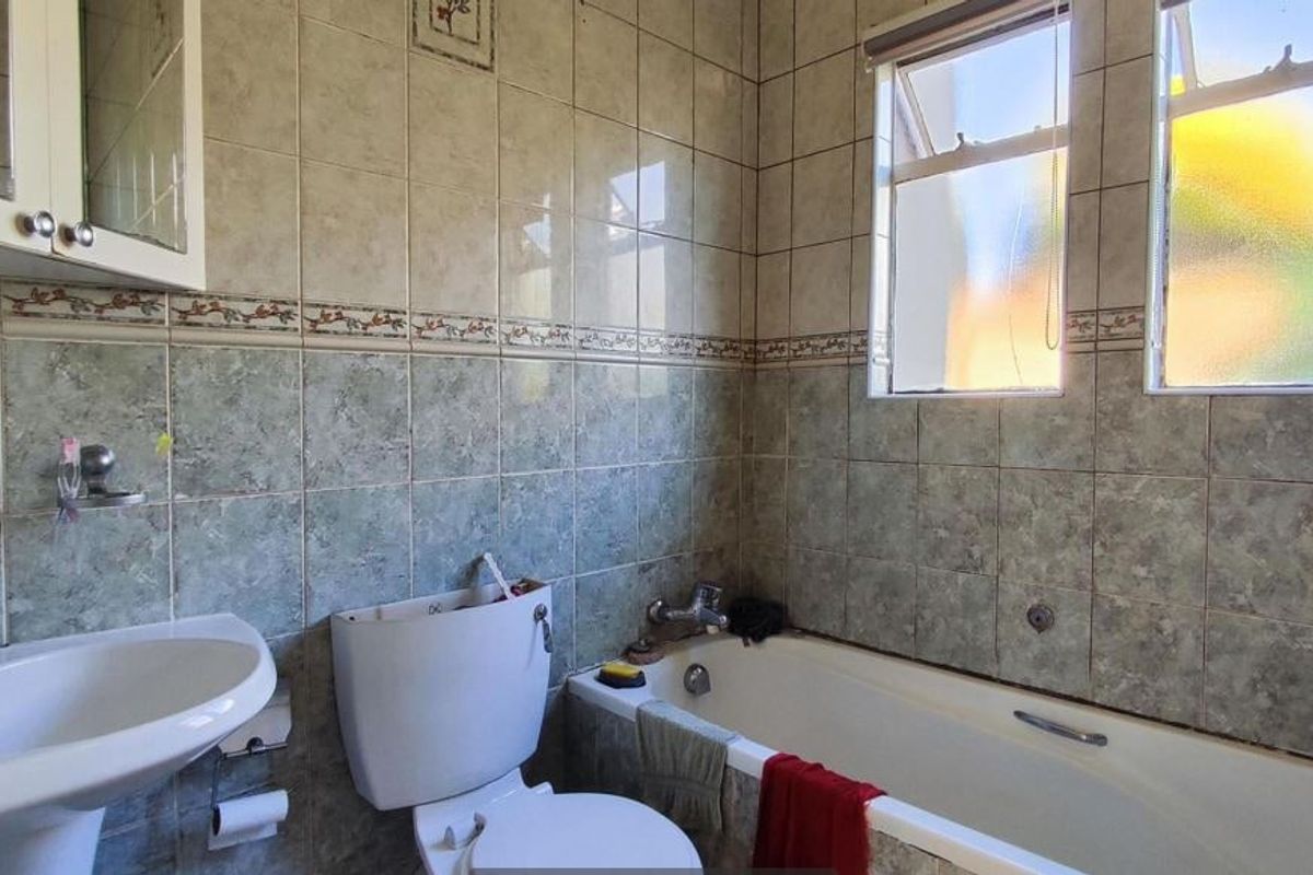 A functional bathroom featuring a pedestal basin, bathtub, and tiled walls. The space is dated and would benefit from modern finishes.