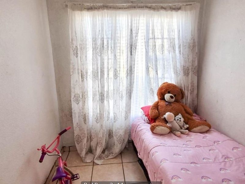 A compact bedroom featuring tiled flooring and a window with curtain rails, currently showing signs of wear on the walls.