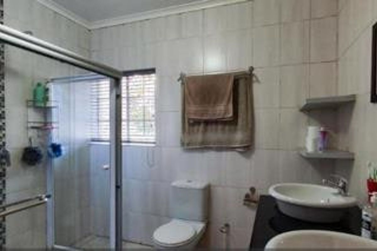 A functional bathroom featuring a shower enclosure, toilet, and vanity basin with tiled walls and window blinds.