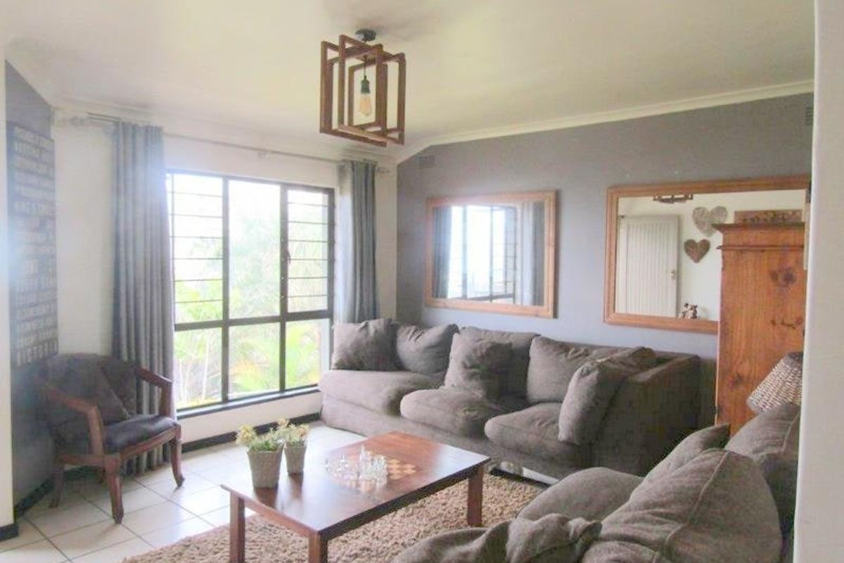A comfortable living room featuring tiled flooring, a large window with security bars, and a modern geometric ceiling light fixture.