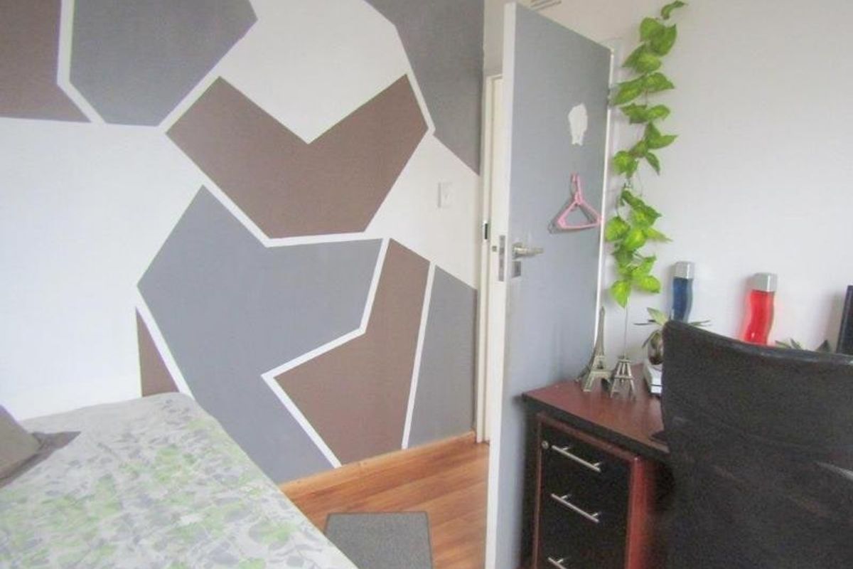 A bedroom featuring laminate flooring and a feature wall with geometric paintwork.