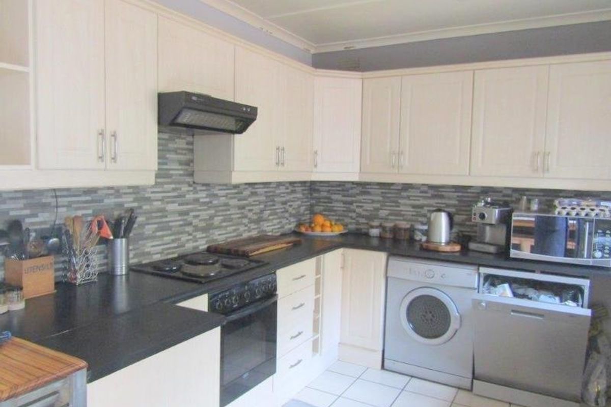 Functional kitchen featuring light-toned cabinetry, dark countertops, tiled backsplash, and integrated appliances including a dishwasher and washing machine.