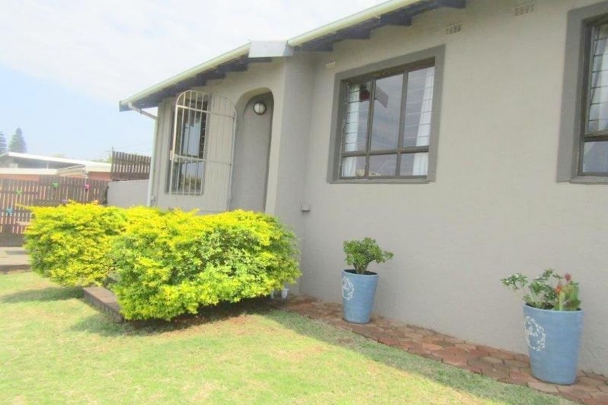 A view of the rear exterior facade featuring a security gate, aluminium window frames, and a paved walkway alongside a small garden area.