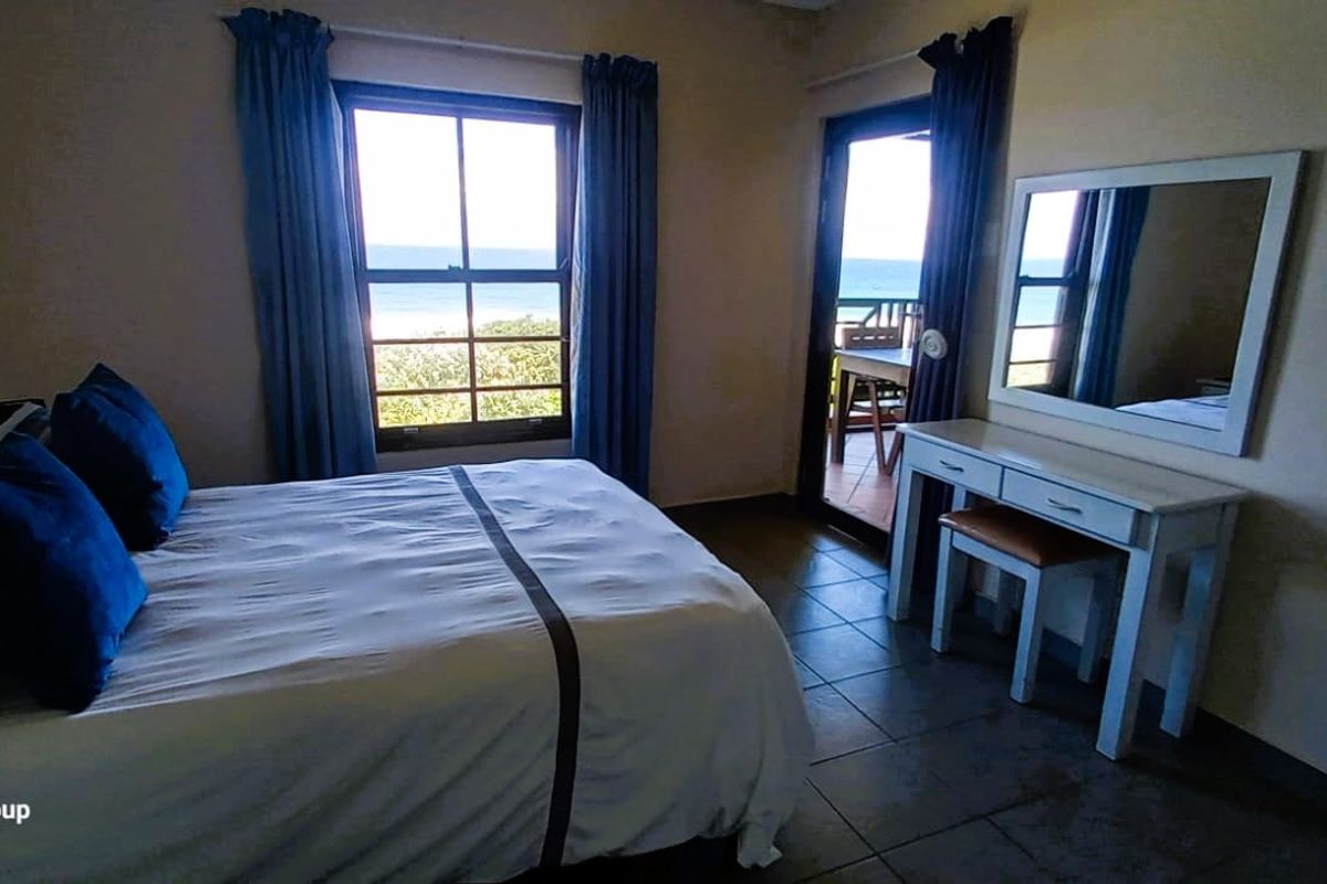A bedroom featuring tiled flooring, a casement window, and a sliding glass door providing access to an outdoor area with ocean views.