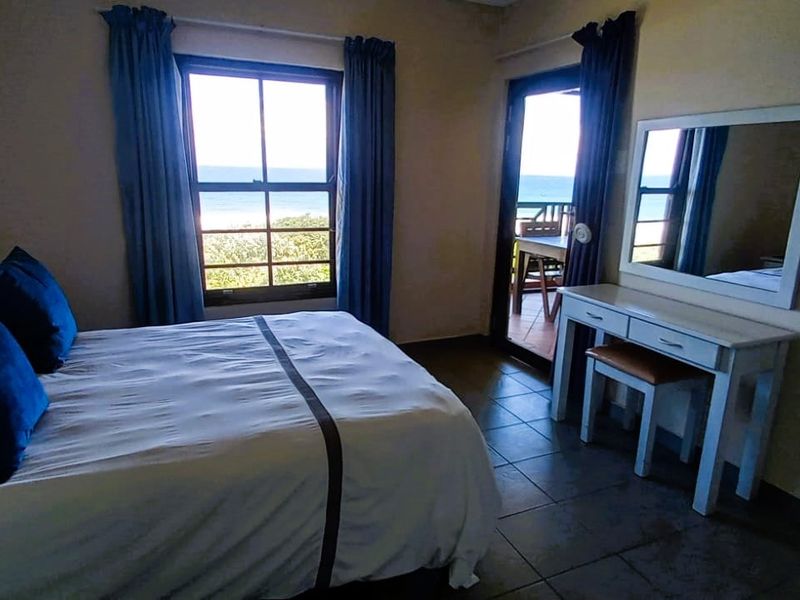 A bedroom featuring tiled flooring, a casement window, and a sliding glass door providing access to an outdoor area with ocean views.